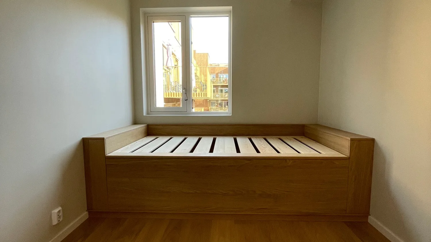 Brisken i eik under vinduet, sett fra rommet, med sengebunnen i furu og glatte fronter i eikefiner.